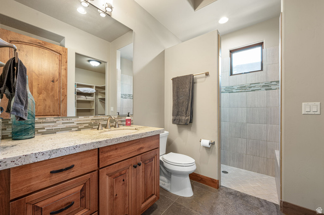 2331 West Entrada Trail, Unit 61 St. George, UT 84770 - Photo 53 of 69 Bathroom featuring a granite-style countertop, wood-finish cabinetry, a tiled shower with a decorative accent band, and a frosted window