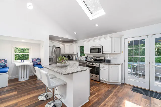 a kitchen with stainless steel appliances kitchen island granite countertop a stove top oven a sink a dining table and chairs with wooden floor