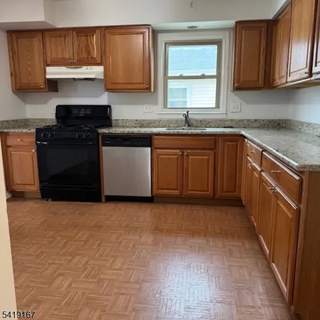 a kitchen with granite countertop a sink a stove top oven and cabinetry