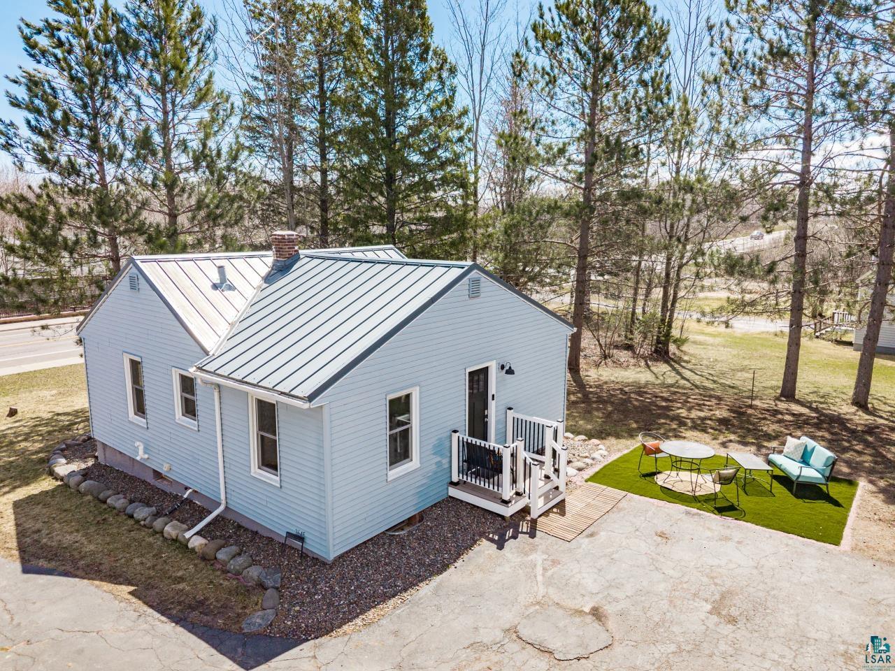 3645 Haines Road Hermantown, MN 55811 - Photo 4 of 35 Light blue siding exterior featuring a metal roof, front porch with white railings, and a small patio area with artificial turf