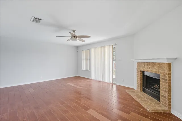 a view of an empty room with wooden floor fireplace and a window
