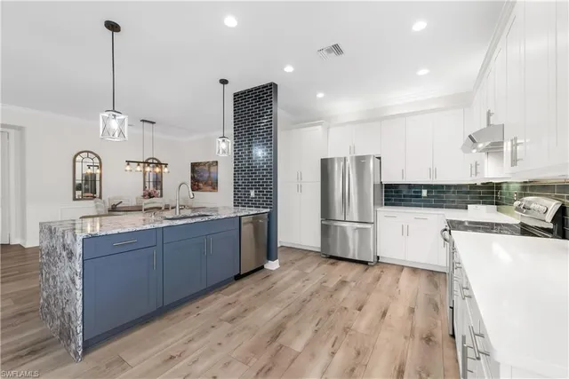 a large kitchen with stainless steel appliances kitchen island granite countertop a refrigerator a sink dishwasher a stove and white cabinets with wooden floor