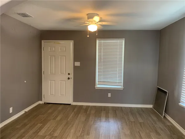 an empty room with wooden floor fan and windows