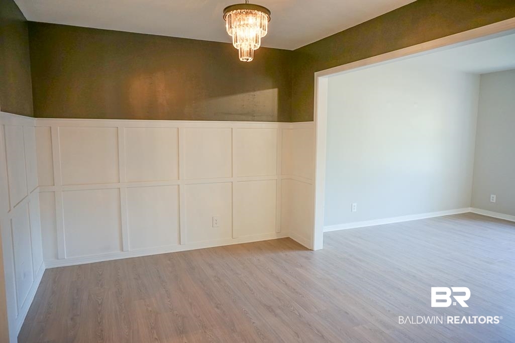 6205 Zeigler Boulevard Mobile, AL 36608 - Photo 5 of 17 Unfurnished room featuring a decorative wall, a chandelier, a wainscoted wall, and wood finished floors