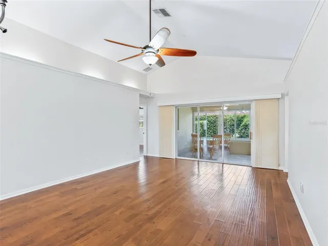 a view of an empty room with wooden floor ceiling fan