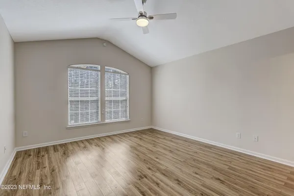 an empty room with wooden floor chandelier fan and windows