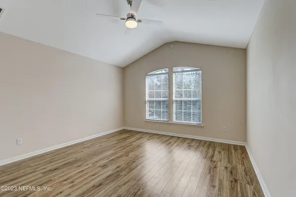 an empty room with wooden floor chandelier fan and windows