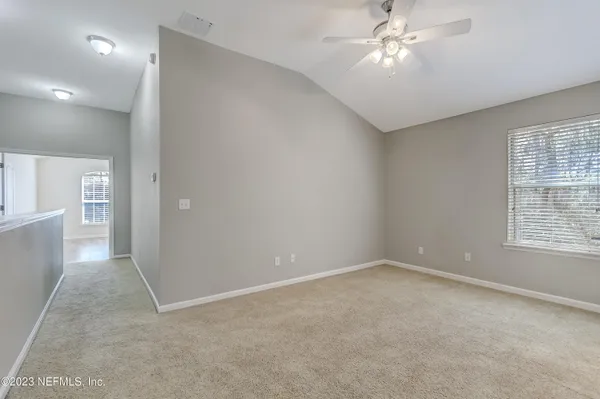 an empty room with chandelier fan and windows
