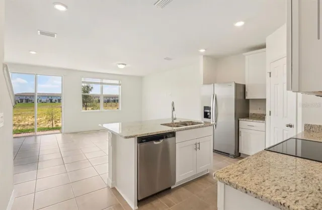 a view of kitchen with granite countertop a refrigerator a sink and white cabinets