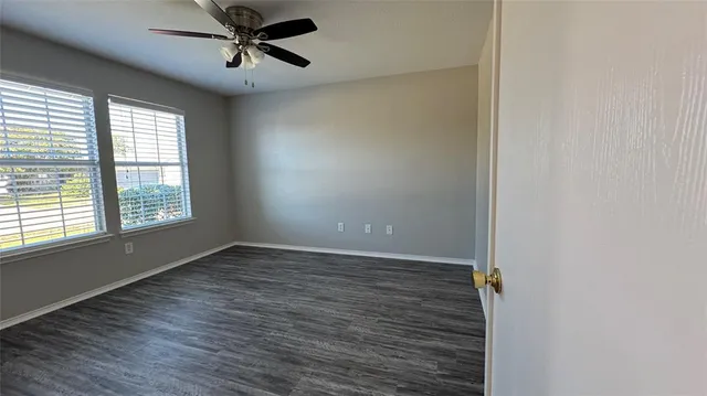 an empty room with wooden floor fan and windows