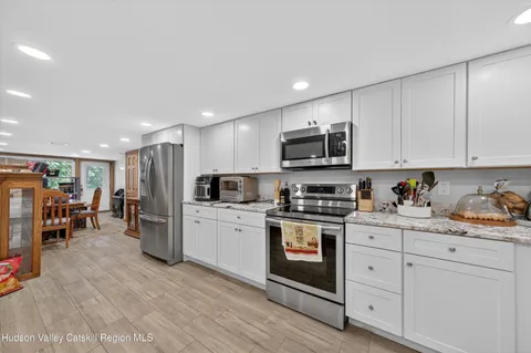 a kitchen with stainless steel appliances granite countertop a refrigerator a stove top oven a sink dishwasher and white cabinets with wooden floor