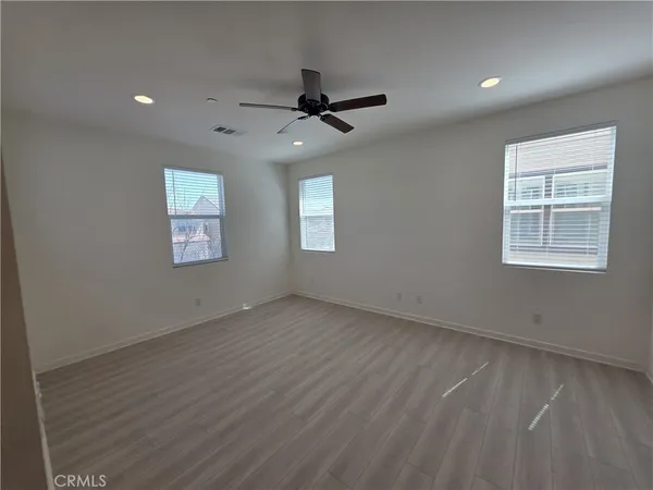 an empty room with wooden floor ceiling fan and windows