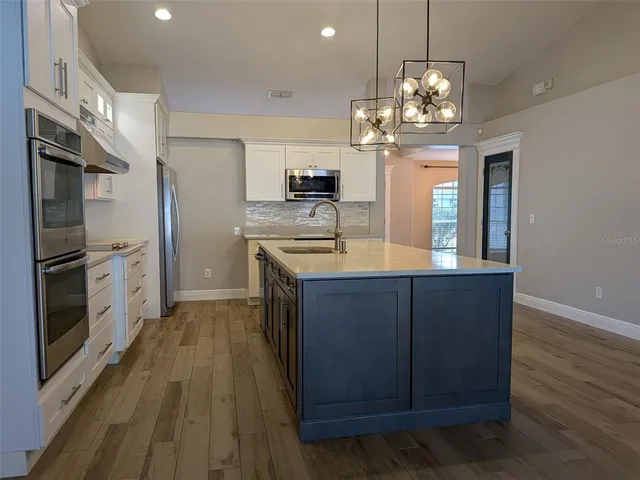 a kitchen with kitchen island granite countertop wooden floors stainless steel appliances a sink and a counter top space