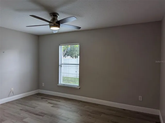 an empty room with wooden floor fan and windows