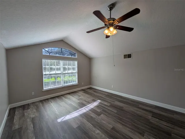 an empty room with wooden floor fan and windows