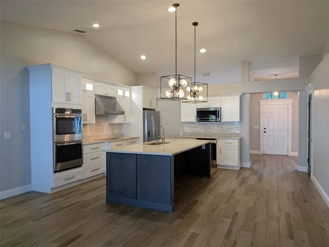 a large kitchen with a center island wooden floor stainless steel appliances and a view of living room