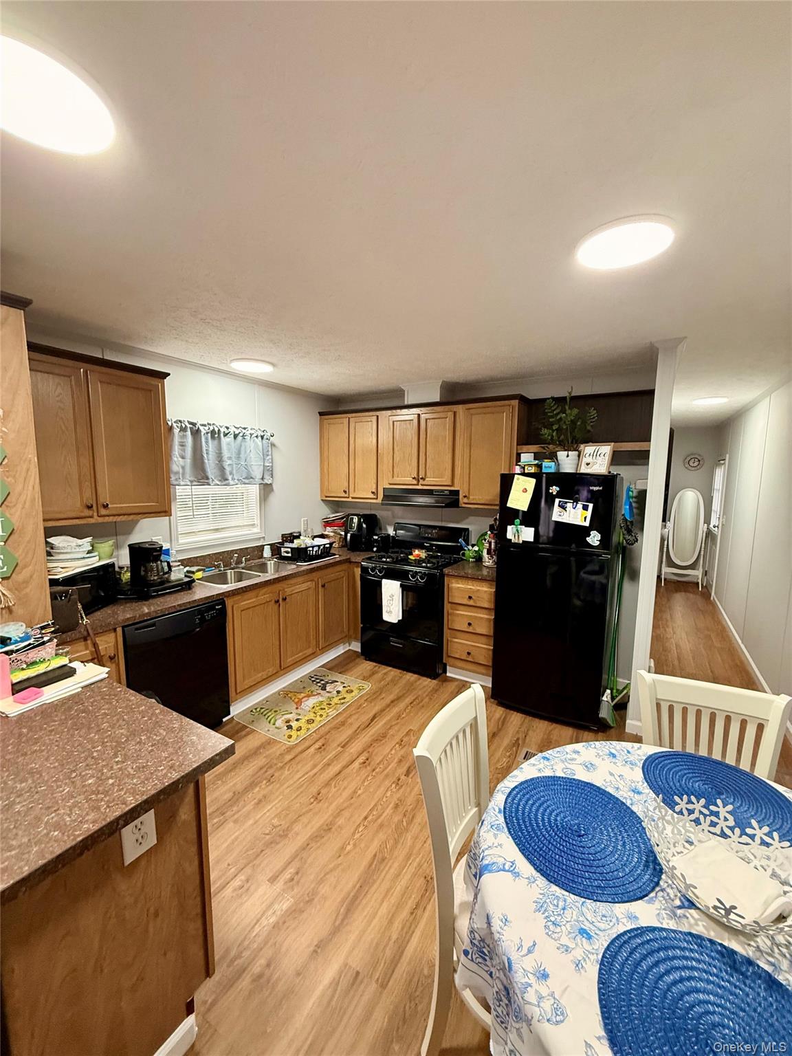 37 Hubbard Avenue, Unit 95 Riverhead, NY 11901 - Photo 8 of 14 Kitchen with light wood-style floors, black appliances, brown cabinetry, and under cabinet range hood