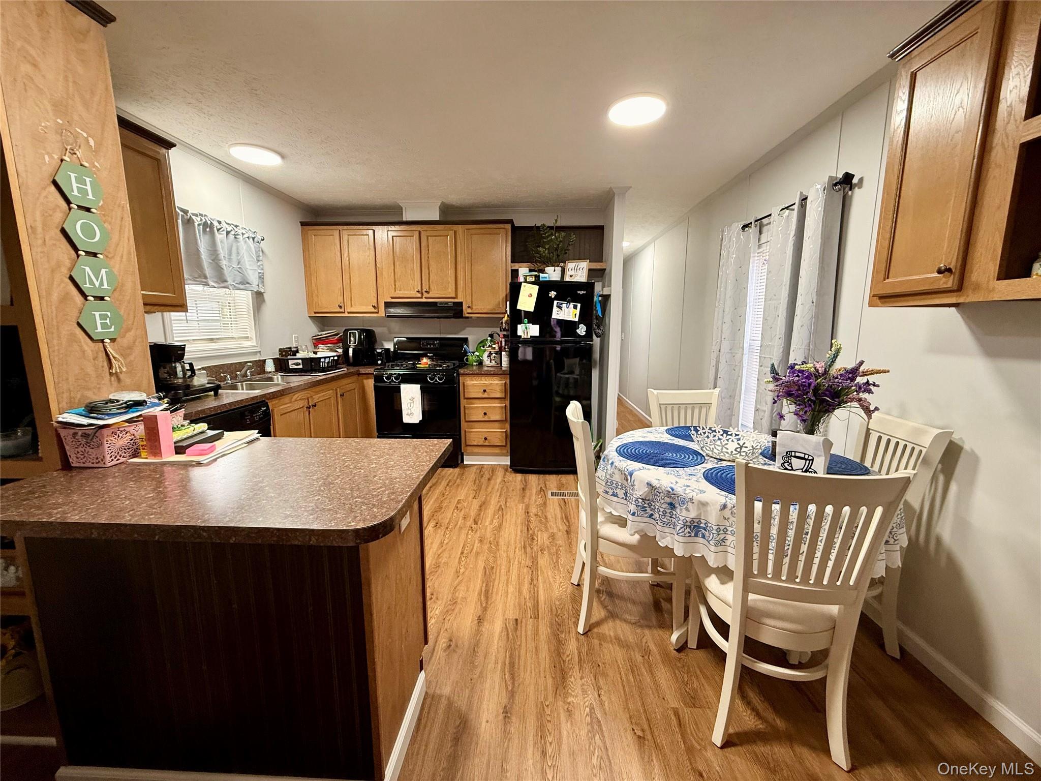 37 Hubbard Avenue, Unit 95 Riverhead, NY 11901 - Photo 9 of 14 Kitchen featuring black appliances, light wood finished floors, a peninsula, dark countertops, and brown cabinetry