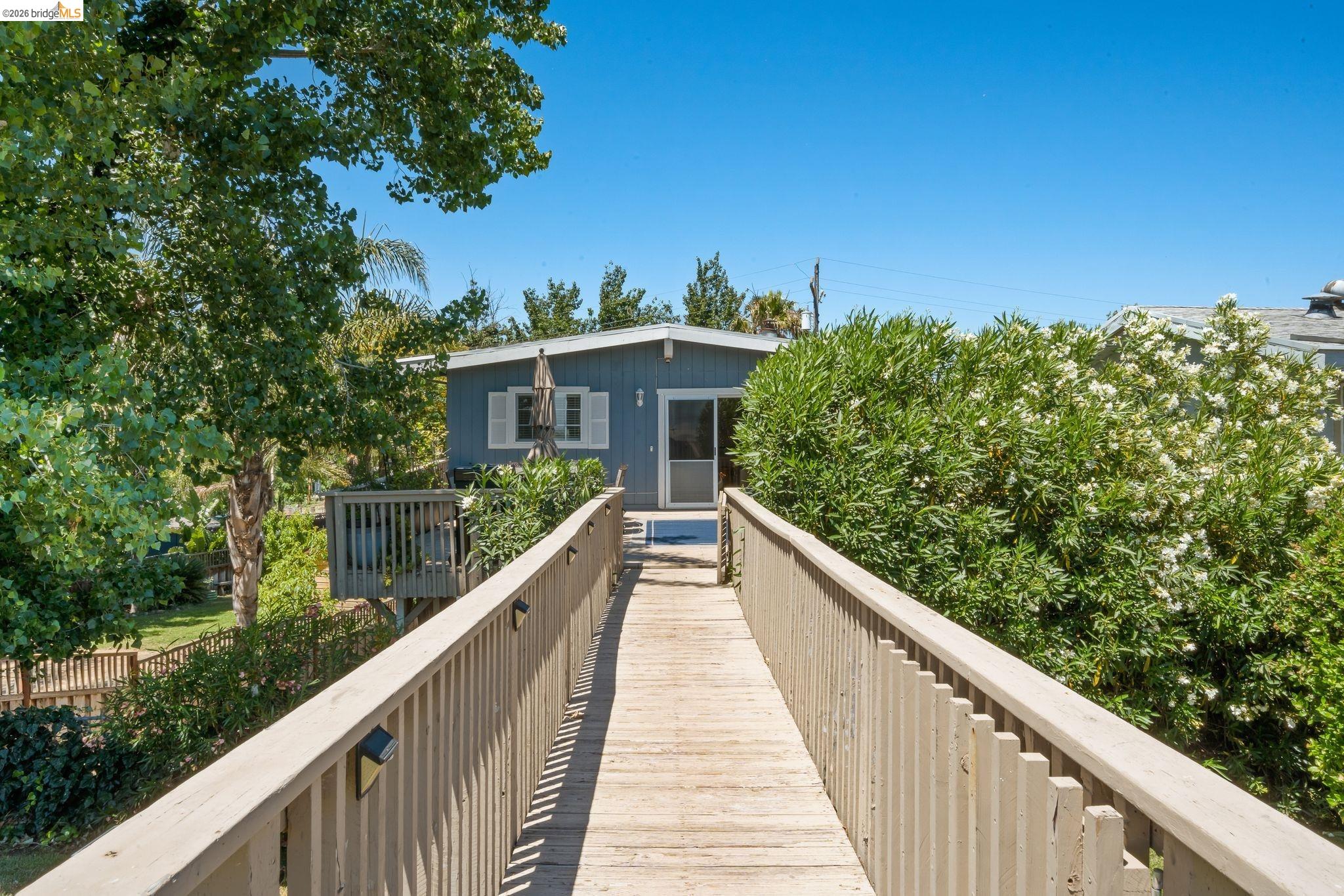 1704 Taylor Road Bethel Island, CA 94511 - Photo 48 of 73 Elevated wood-finish walkway providing access to a property featuring a light blue exterior, white window shutters, and a sliding glass door