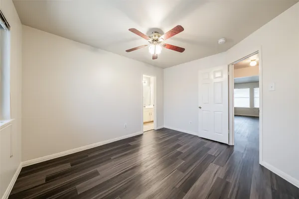 a view of an empty room with wooden floor and a ceiling fan