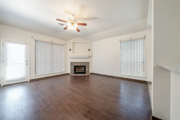 an empty room with wooden floor fireplace and windows
