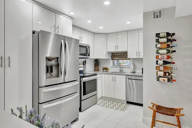 a kitchen with stainless steel appliances kitchen island granite countertop a refrigerator a stove a oven with white cabinets and chairs