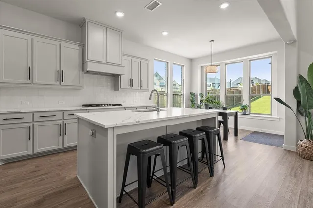 a kitchen with stainless steel appliances granite countertop a stove a refrigerator a sink dishwasher and white cabinets with wooden floor next to windows