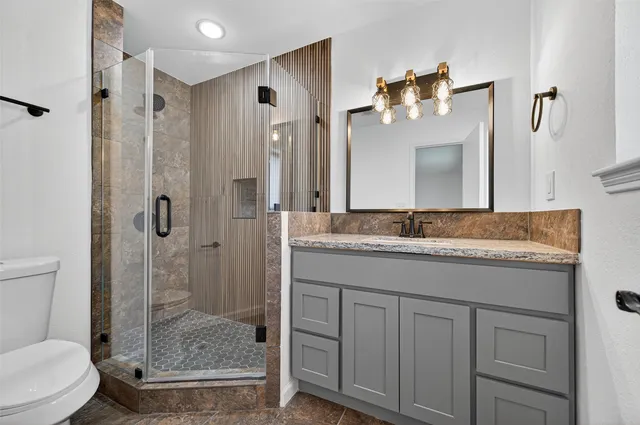 a bathroom with a granite countertop sink a toilet and shower