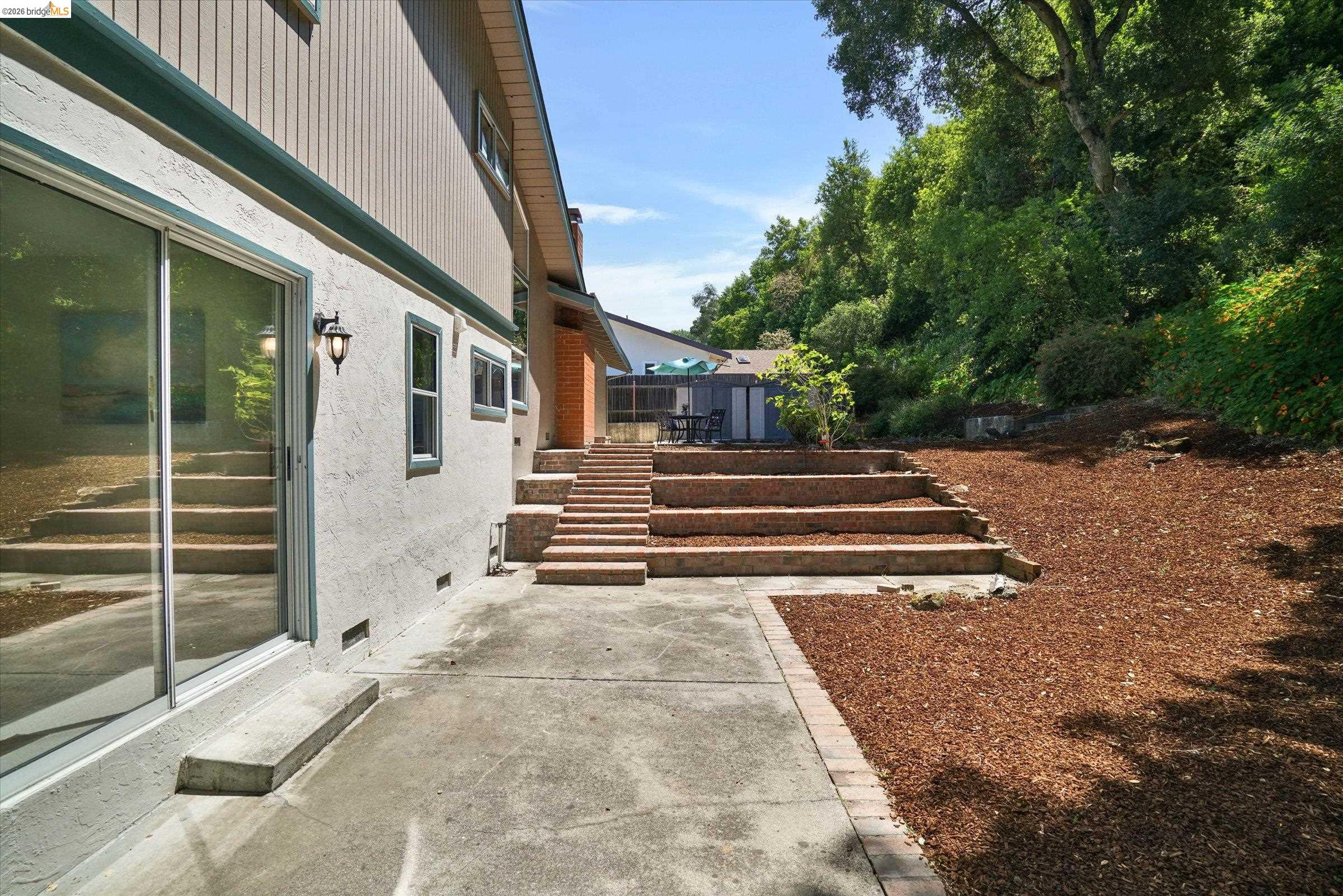2826 Wright Avenue Pinole, CA 94564 - Photo 52 of 70 Concrete patio with brick trim, tiered brick steps, sliding glass door access, and a sloped, mulched landscape area