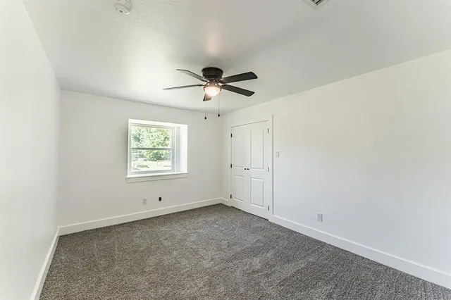 an empty room with ceiling fan and windows