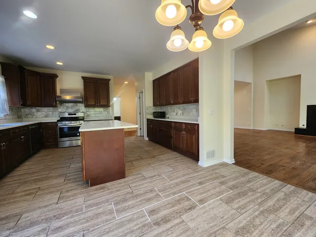 a large kitchen with stainless steel appliances granite countertop a stove top oven a sink dishwasher a dining table and chairs with wooden floor