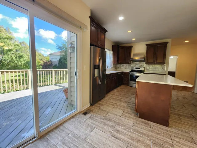 a kitchen with stainless steel appliances granite countertop a refrigerator a sink dishwasher a stove and white countertops with wooden floor