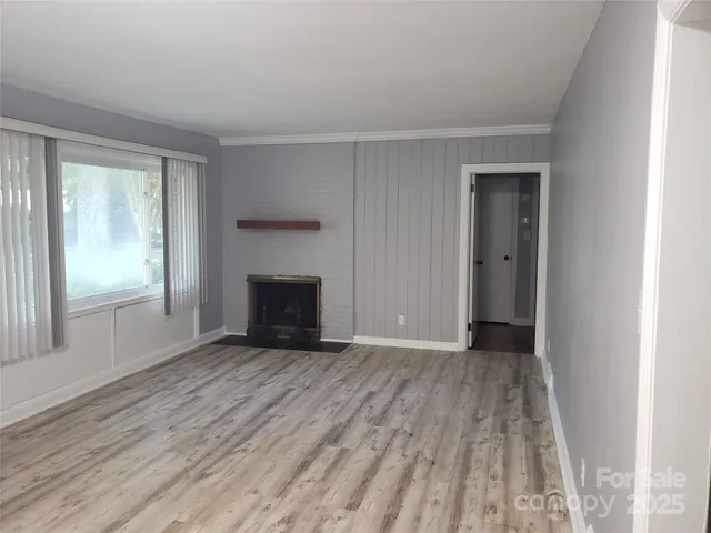 a view of an empty room with wooden floor fireplace and a window