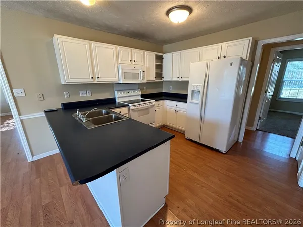 a kitchen with granite countertop a refrigerator a sink and white cabinets