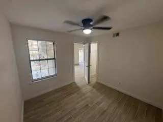 an empty room with wooden floor fan and windows