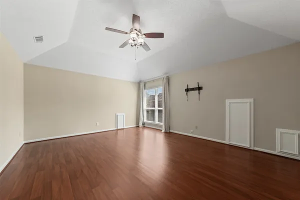 a view of an empty room with wooden floor and a ceiling fan