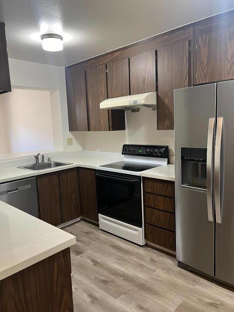 a kitchen with kitchen island granite countertop a stove a refrigerator and a sink with wooden cabinet