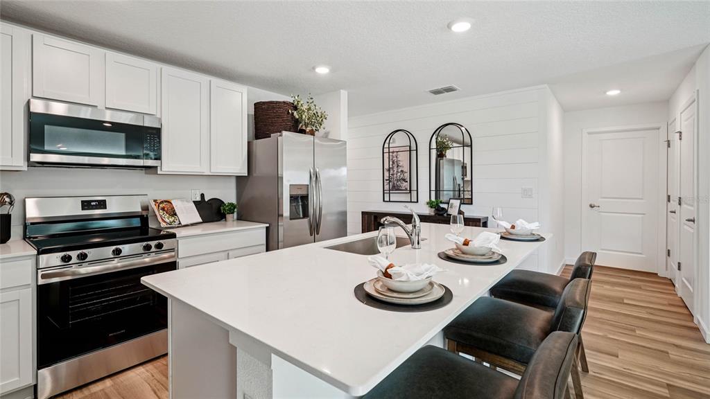 4026 Kona Circle Spring Hill, FL 34608 - Photo 3 of 26 a kitchen with stainless steel appliances kitchen island granite countertop a dining table and chairs with wooden floor