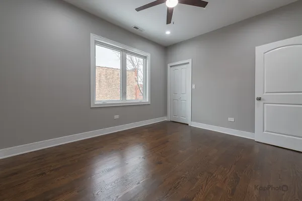 an empty room with wooden floor chandelier fan and windows