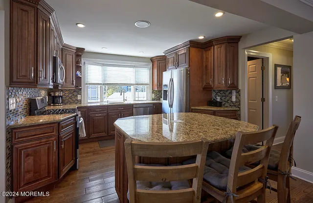 a dining hall with stainless steel appliances granite countertop a stove a sink a dining table and chairs with wooden floor