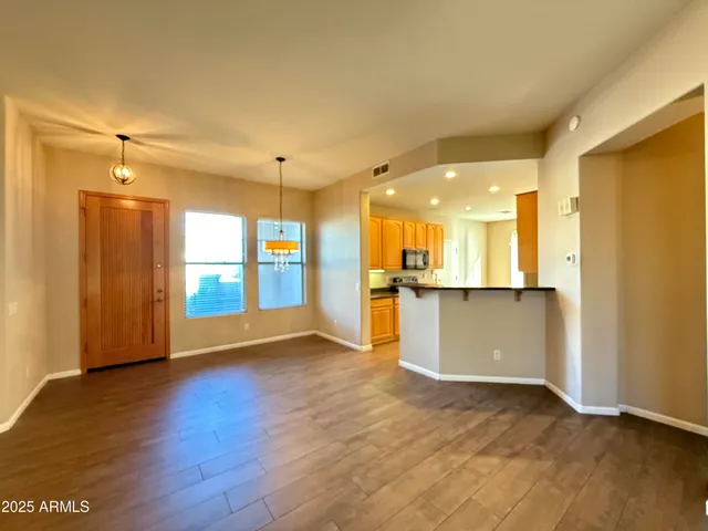 a view of an empty room and kitchen with wooden floor