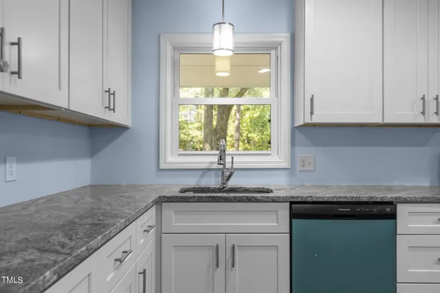 a kitchen with granite countertop a sink stainless steel appliances white cabinets and a window
