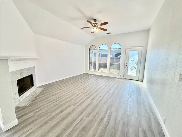 a view of an empty room with wooden floor fireplace and a window