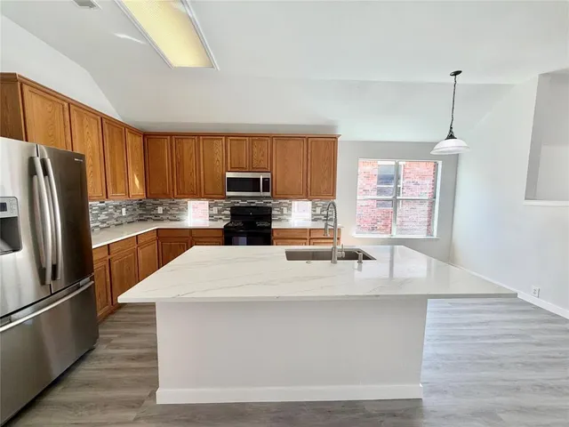 a large kitchen with granite countertop a refrigerator a stove a sink a center island and wooden floor