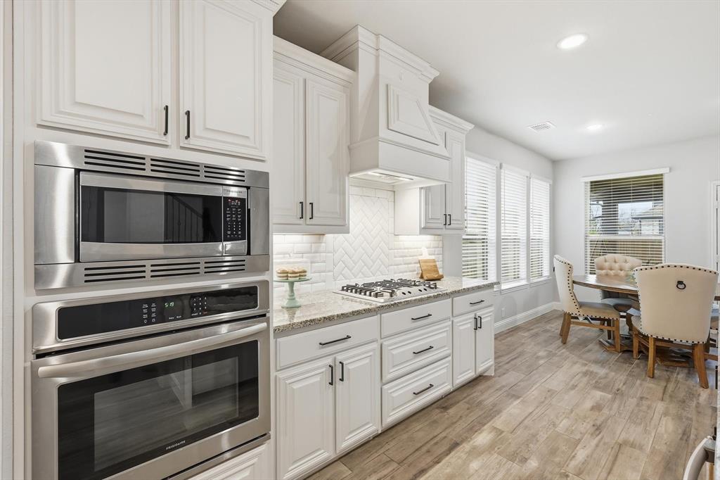 924 Timber Ridge Drive Justin, TX 76247 - Photo 11 of 32 Gourmet kitchen showcasing a built-in stainless steel microwave and oven, a gas cooktop, white shaker cabinetry with dark hardware, a herringbone tile backsplash, and light-toned wood-finish flooring