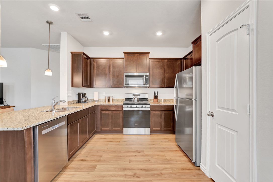 909 Davy Street Brenham, TX 77833 - Photo 13 of 35 Kitchen with stainless steel appliances, light stone countertops, light wood-type flooring, dark wood finish cabinetry, and hanging light fixtures