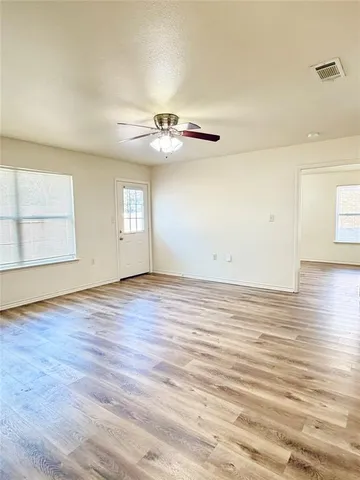 an empty room with wooden floor chandelier fan and windows