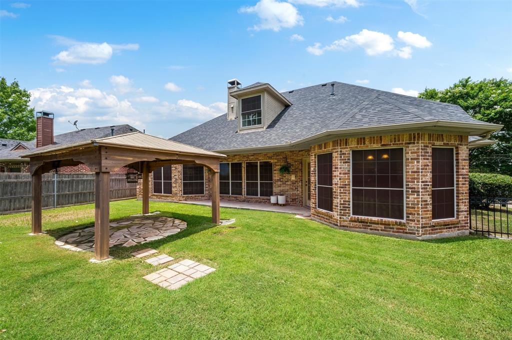 5607 Ranger Drive Rockwall, TX 75032 - Photo 36 of 40 Spacious backyard featuring a wooden gazebo with a stone patio, mature green lawn, and a brick exterior home with multiple windows