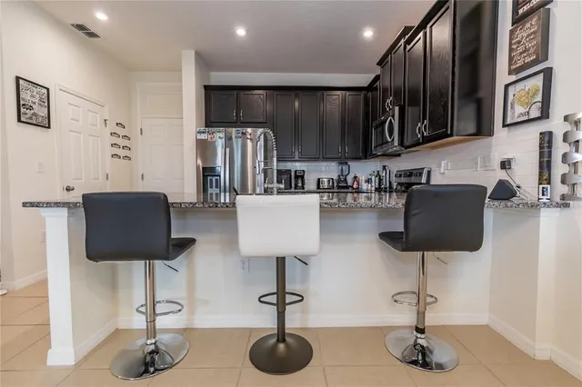 a kitchen with stainless steel appliances kitchen island granite countertop a table chair and a refrigerator