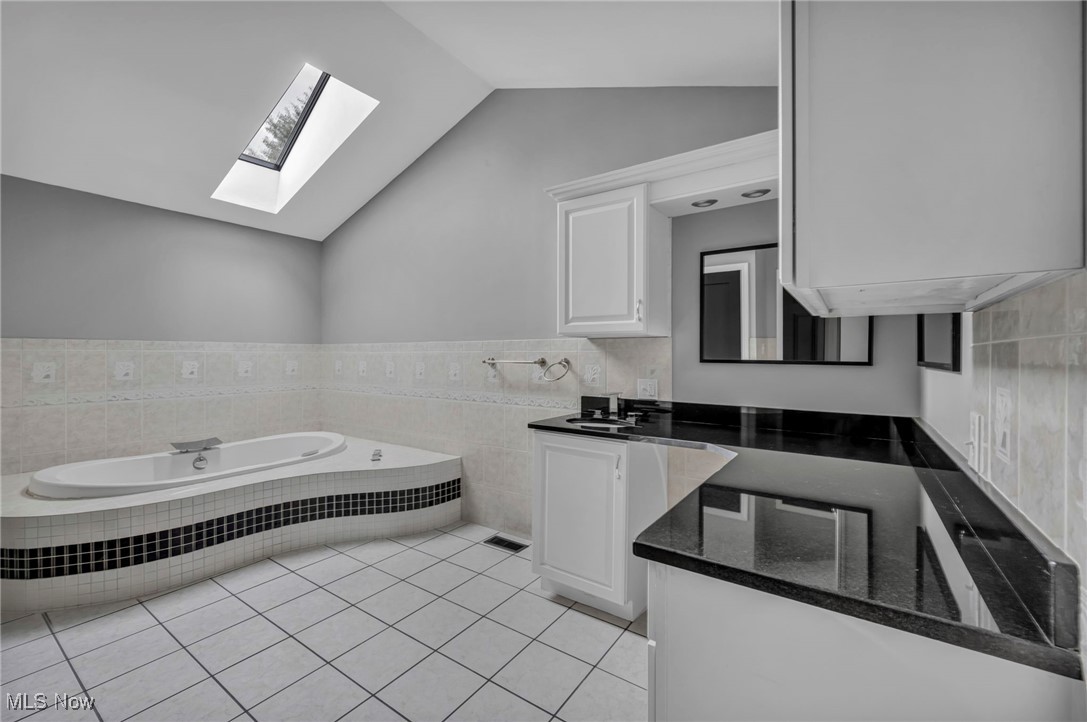 20202 Sumpter Road Cleveland, OH 44128 - Photo 25 of 46 Full bathroom with lofted ceiling, vanity, a bath, light tile patterned floors, and tile walls